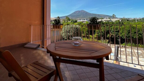 A balcony with a wooden table and chairs, a glass bowl, and a view of a mountain.