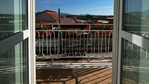 A balcony with a metal railing, a clear blue sky, and a distant view of buildings and mountains.