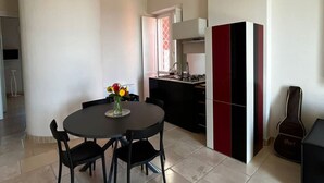 A modern kitchen with a dining area, featuring a round table with chairs, a vase with flowers, and a guitar.