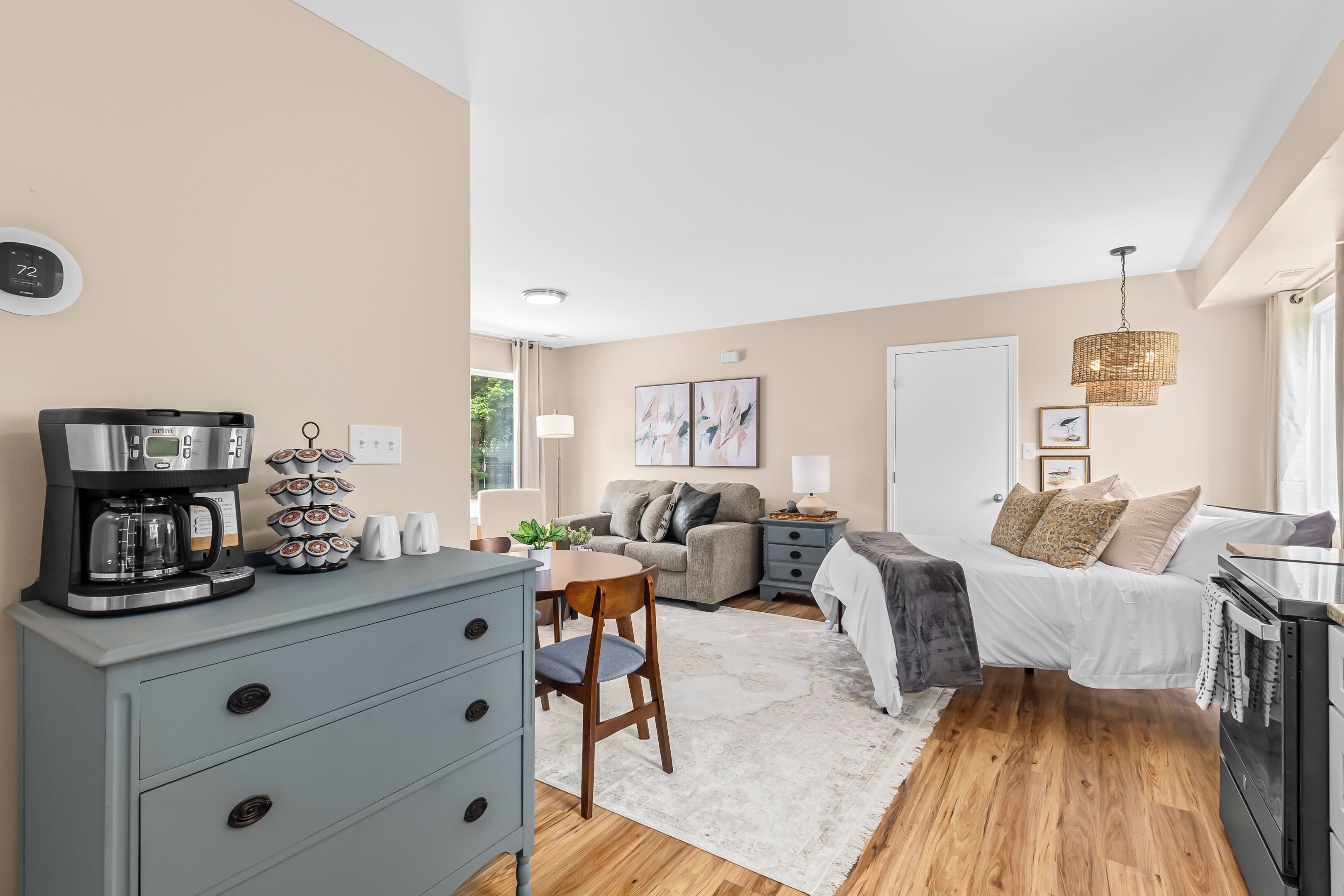 A modern bedroom with a bed, a coffee machine, a dresser, and a desk.