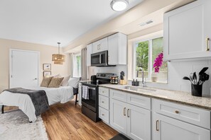 A modern kitchen with white cabinets, a black stove, and a window with a view of greenery. - New! Comfy & Cozy Private Studio Flat (Roseville)