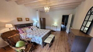 Een slaapkamer met een bed, een schommelstoel, een nachtkastje met een lamp, een dressoir en een spiegel.