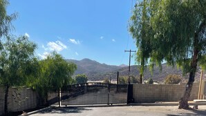A paved parking area with a gated entrance, a brick wall, and a tree. - Guest house at a private resort in Good Hope Area (Perris)