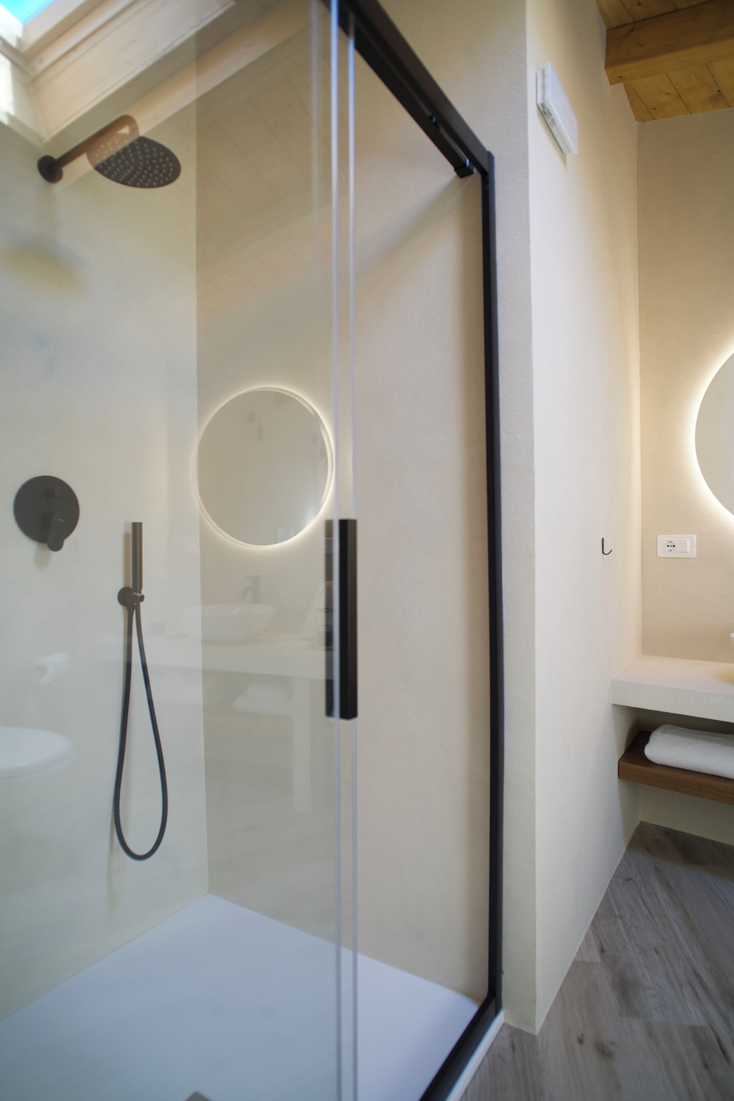 A modern bathroom with a glass-enclosed shower, a round mirror with integrated lighting, and a wooden vanity.