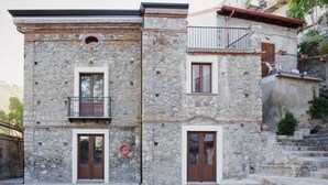 A stone building with two windows and a door, a balcony, and a small circular window. - Casa Marinari (Scalea)