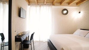 A bedroom with a bed, a desk with chairs, a television, and a window with curtains. - Casa Marinari (Scalea)