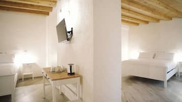 Una habitación con cama, una mesita con tetera y televisor en la pared.