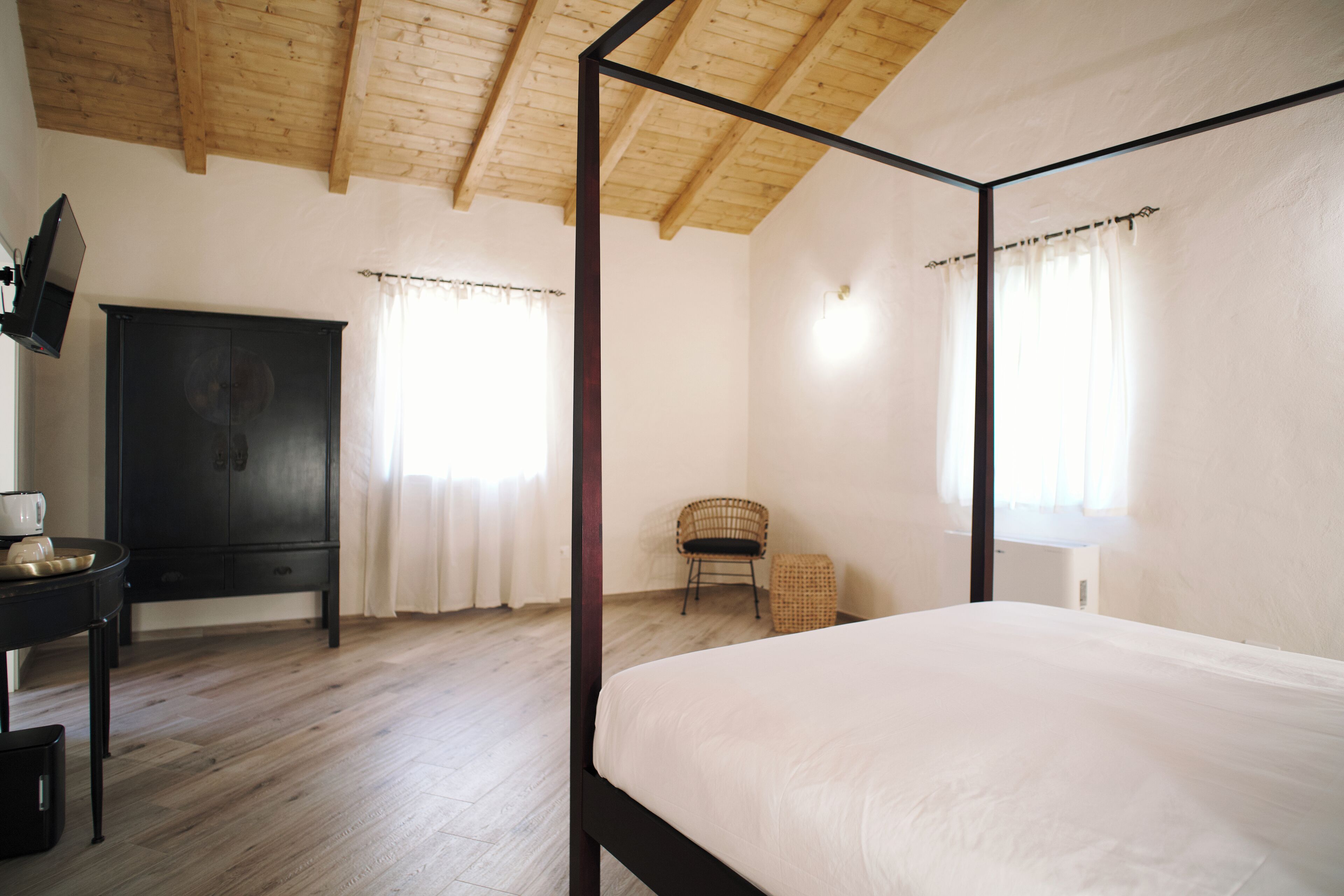 Un dormitorio con cama con dosel, techo de madera, armario negro y silla de mimbre.