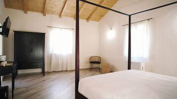 Un dormitorio con cama con dosel, techo de madera, armario negro y silla de mimbre.