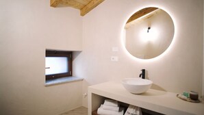 Un baño moderno con un espejo ovalado grande, un lavamanos blanco, una ventana pequeña y un perchero para toallas.