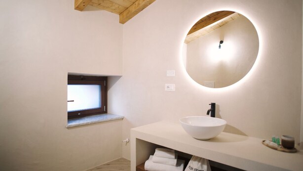 A modern bathroom with a large oval mirror, a white sink, a small window, and a towel rack. - Casa Marinari (Scalea)