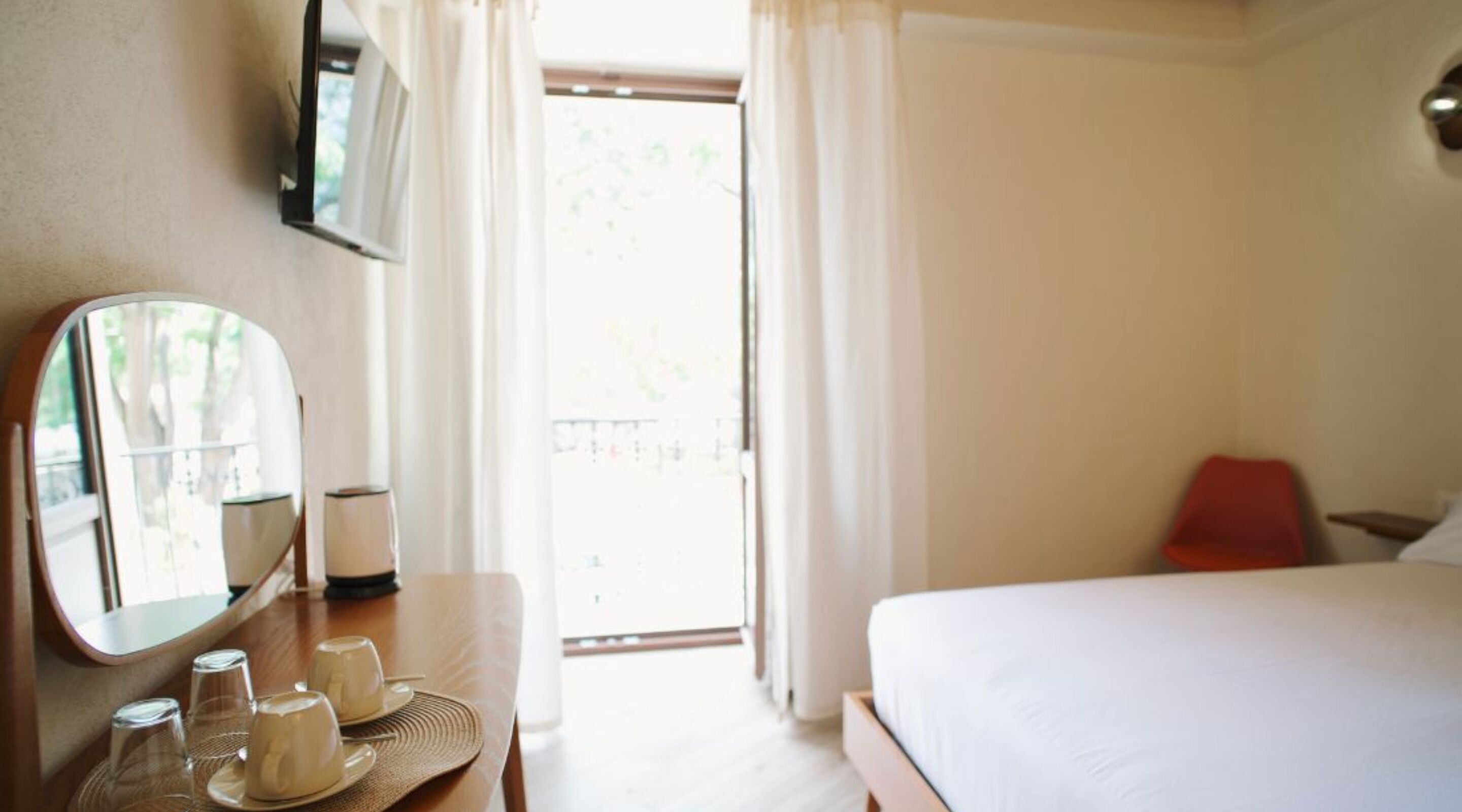 Habitación de hotel con cama, mesita de noche con espejo, lámpara y vistas al exterior.