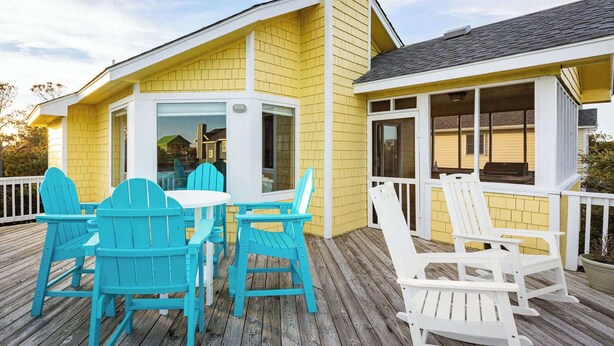 Un bâtiment jaune doté d’une terrasse en bois, avec un espace extérieur aménagé avec des chaises et une table.