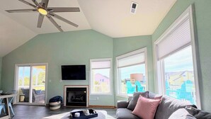 Un salon doté d’un ventilateur de plafond, d’une cheminée, d’un téléviseur fixé au mur et de grandes fenêtres équipées de stores.