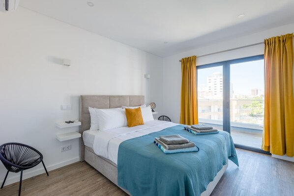 A modern hotel room with a large bed, a view of the city, and a bright yellow curtain.