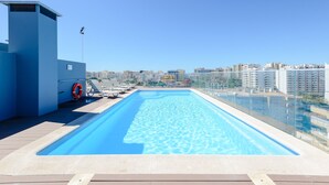 Une piscine sur le toit, avec une eau d’un bleu cristallin, entourée d’une rambarde en verre, et offrant une vue panoramique sur la ville et ses gratte-ciel.