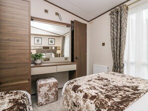 A bedroom with a wooden wardrobe, a bed with a patterned duvet, a bedside table with a plant, and a large mirror above the dresser. - 43 Pony Meadow (Windermere)