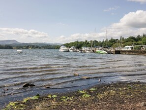 A lakeside marina with boats docked, a rocky shoreline, and a backdrop of hills and trees. - 43 Pony Meadow (Windermere)