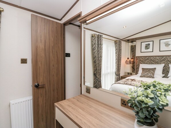 A bedroom with a wooden door, a bedside table, a mirror reflecting the bed, and a potted plant. - 43 Pony Meadow (Windermere)