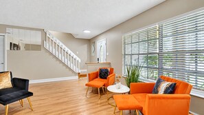 Ein Wohnzimmer mit Treppe, orangefarbigen Möbeln und einem großen Fenster mit Jalousien.