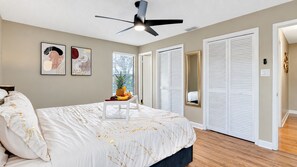 A bedroom with a bed, a ceiling fan, a bedside table with fruit, and a closet with sliding doors.