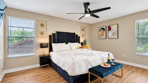 Ein Schlafzimmer mit einem Bett, Nachttischen, einem Deckenventilator, Kunstwerken an den Wänden und einem Fenster mit Jalousien.
