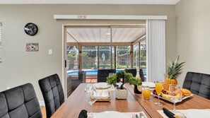 A dining area with a table set for four, a clock on the wall, and a view of a swimming pool outside.