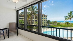 A balcony with a view of a swimming pool, palm trees, and a building in the background. - Everything is New! Immaculate Beach Front Condo with Stunning Views at Island Reef, 304A (Siesta Key)