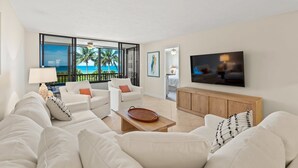 A modern living room with a large TV, white furniture, and a view of the ocean. - Everything is New! Immaculate Beach Front Condo with Stunning Views at Island Reef, 304A (Siesta Key)