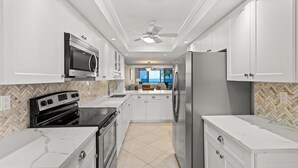 A modern kitchen with white cabinets, a stainless steel refrigerator, a microwave, and a stove. - Everything is New! Immaculate Beach Front Condo with Stunning Views at Island Reef, 304A (Siesta Key)