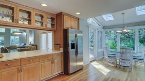 A modern kitchen with wooden cabinets, a stainless steel refrigerator, and a dining area with white chairs and a glass table. - 12 Haul Away - 5 Bedroom - Private Pool, Lagoon View Short Walk to the Beach (Hilton Head)