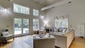A spacious living room with a large sofa, a coffee table, and a dining area. There are multiple windows providing natural light and views of the outdoors. - 12 Haul Away - 5 Bedroom - Private Pool, Lagoon View Short Walk to the Beach (Hilton Head)