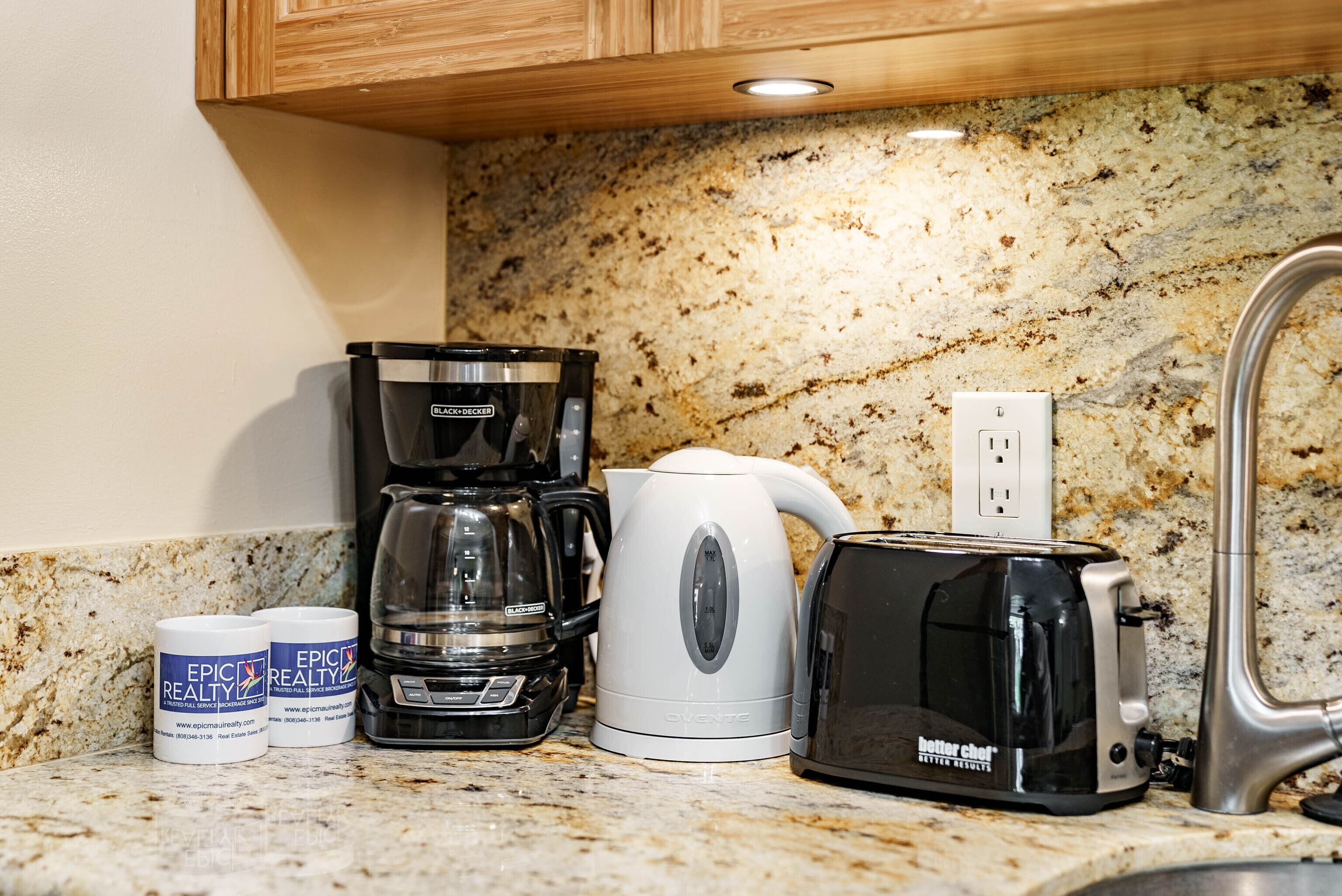 A kitchen with a granite countertop, a coffee maker, a kettle, a toaster, and two containers labeled "Epic Realty".