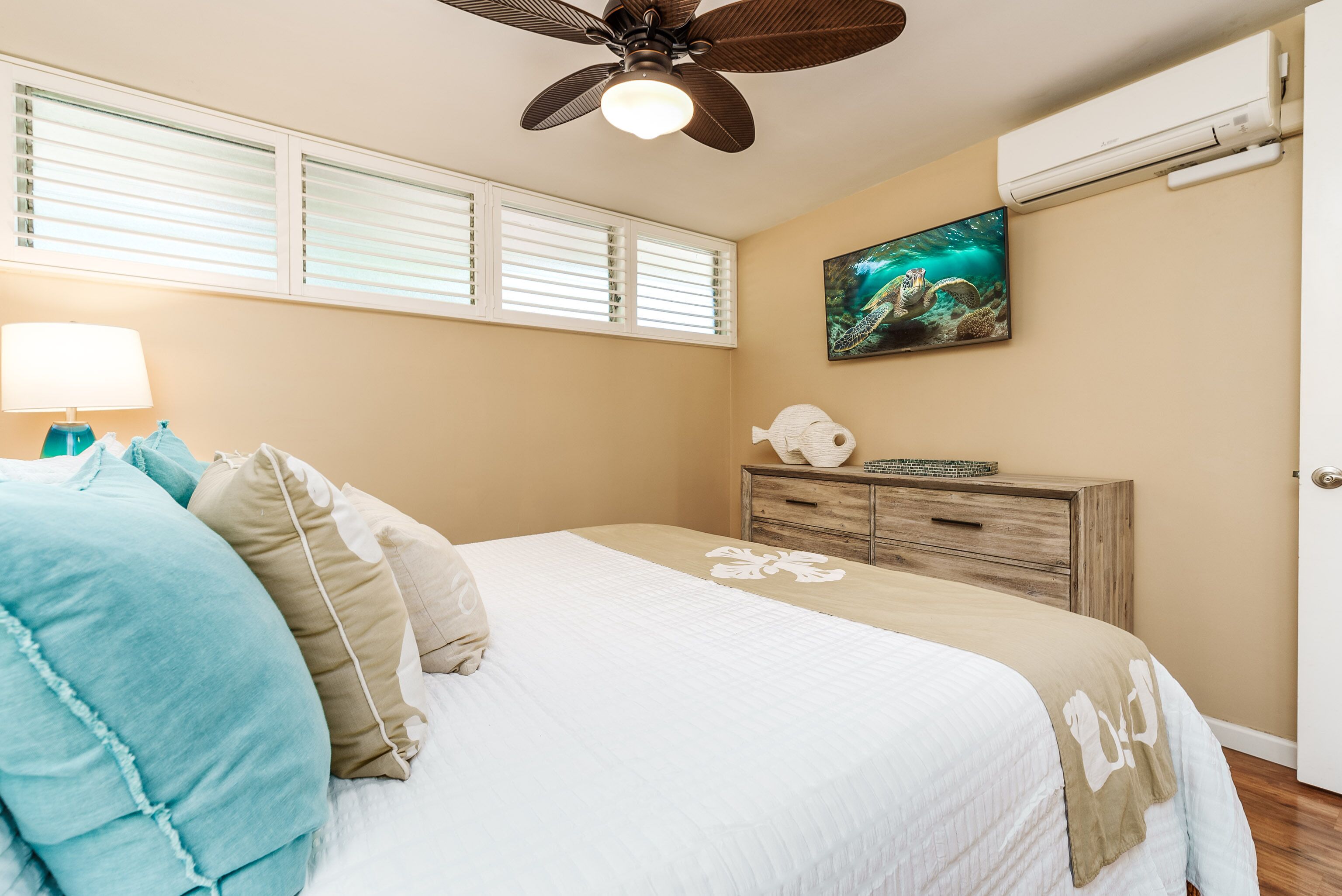 Ein Schlafzimmer mit Bett, Deckenventilator, Klimaanlage, Fenster mit Jalousien und einem Bild an der Wand.