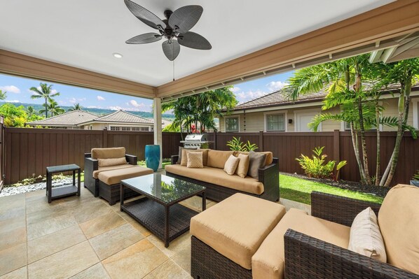 Patio esterno con mobili in vimini, una ventola a soffitto e vista su una zona residenziale.