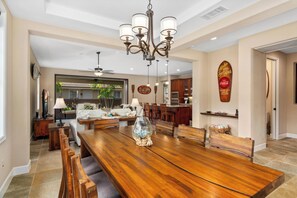 Un'ampia sala da pranzo con tavolo e sedie in legno, un lampadario e vista sulla cucina e sul soggiorno sullo sfondo.