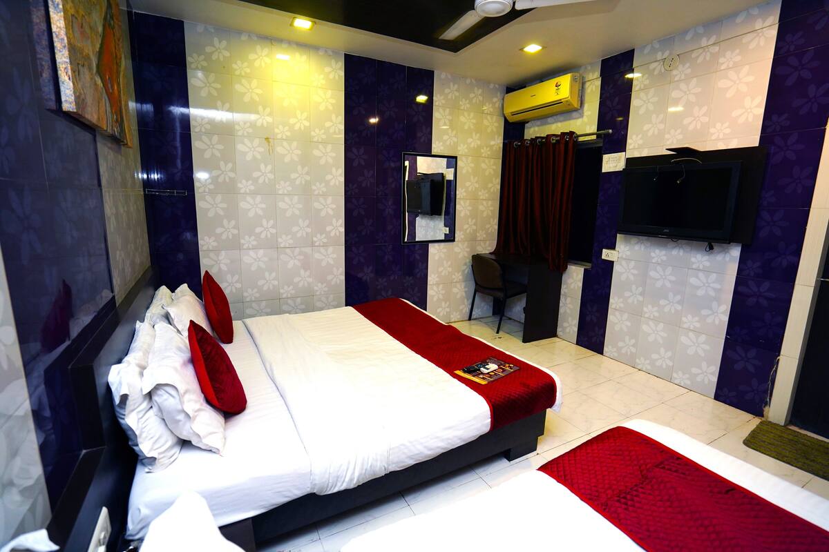 A hotel room with a large bed, a TV mounted on the wall, and a desk with a chair.