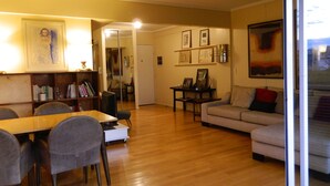 A living room with a wooden floor, a sofa, a dining table with chairs, and a bookshelf. - Outstanding apartment with amazing views in heart of Palermo verde (Buenos Aires)