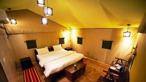 A bedroom with a bed, bedside tables, a small table, a chair, and a red and yellow striped rug. - Sukoon Retreat Dakpathar  (Vikasnagar)