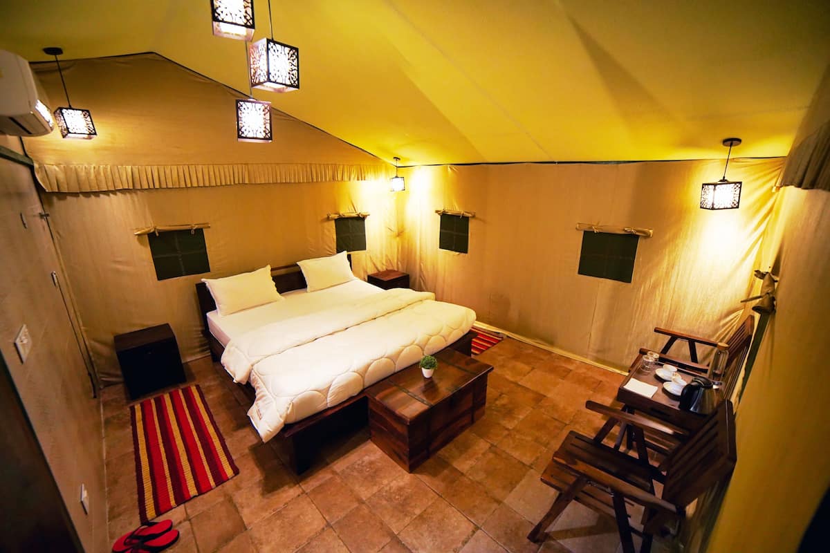 A bedroom with a bed, bedside tables, a small table, a chair, and a red and yellow striped rug.