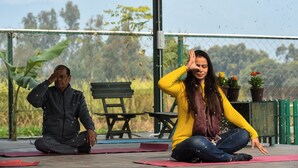 Two people sitting on yoga mats outdoors with a fence and chairs in the background. - Sukoon Retreat Dakpathar  (Vikasnagar)