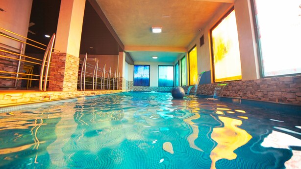 An indoor swimming pool with clear water, stone walls, and a view of the sky through large windows. - Sukoon Retreat Dakpathar  (Vikasnagar)