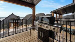 A balcony with a grill, a view of neighboring houses, and a wooden deck.