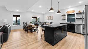 A modern kitchen with a central island, black cabinetry, stainless steel appliances, and a dining area with wooden chairs and a table.
