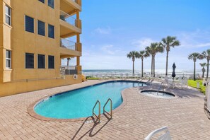A swimming pool with a view of the ocean, surrounded by palm trees and a building with balconies.