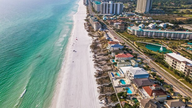 An aerial view of a coastal resort with a long beachfront, high-rise hotels, and a pool area.