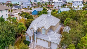 A coastal residential area with a prominent house featuring a unique roof design, surrounded by lush greenery and a view of the sea.