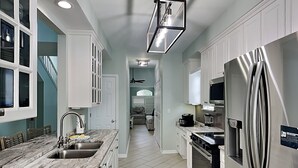 A modern kitchen with white cabinets, a marble countertop, stainless steel appliances, and a staircase leading to another level.