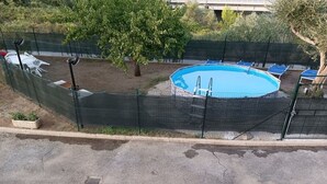 A fenced swimming pool with a ladder, surrounded by a green fence, and a tree nearby. - The little house among the olive trees (Pieve A Elici)