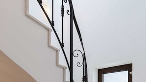 A staircase with a black wrought iron railing, a light fixture, and a window with a view.